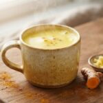 Warm turmeric-ginger milk in a ceramic mug with fresh turmeric, ginger, cinnamon and black pepper – natural joint pain remedy backed by research
